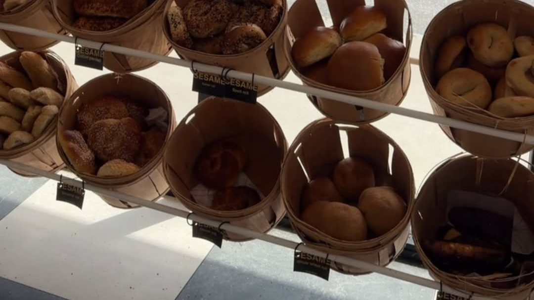 Baskets of bagels and rolls hanging on a rack with Sesame name tags